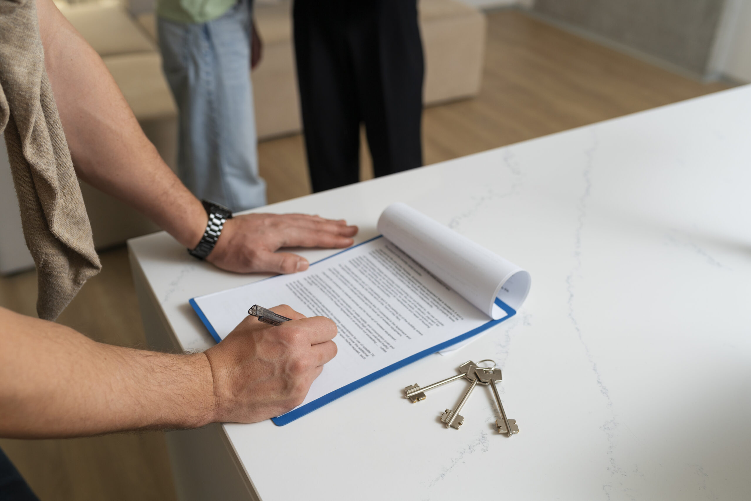 Person signing a tenancy agreement on a clipboard with house keys on the counter.
